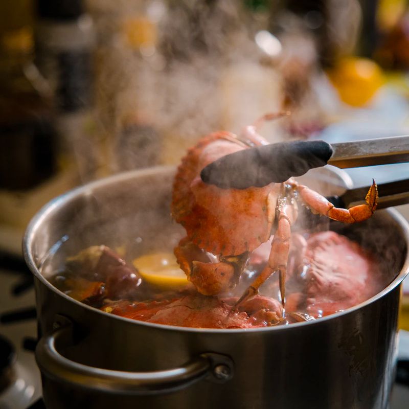 Tongs lifting a crab out of a steaming boil pot