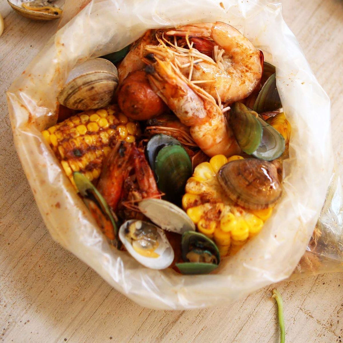 Green mussels, clams, shrimp and corn in an opened boil bag on a wooden table