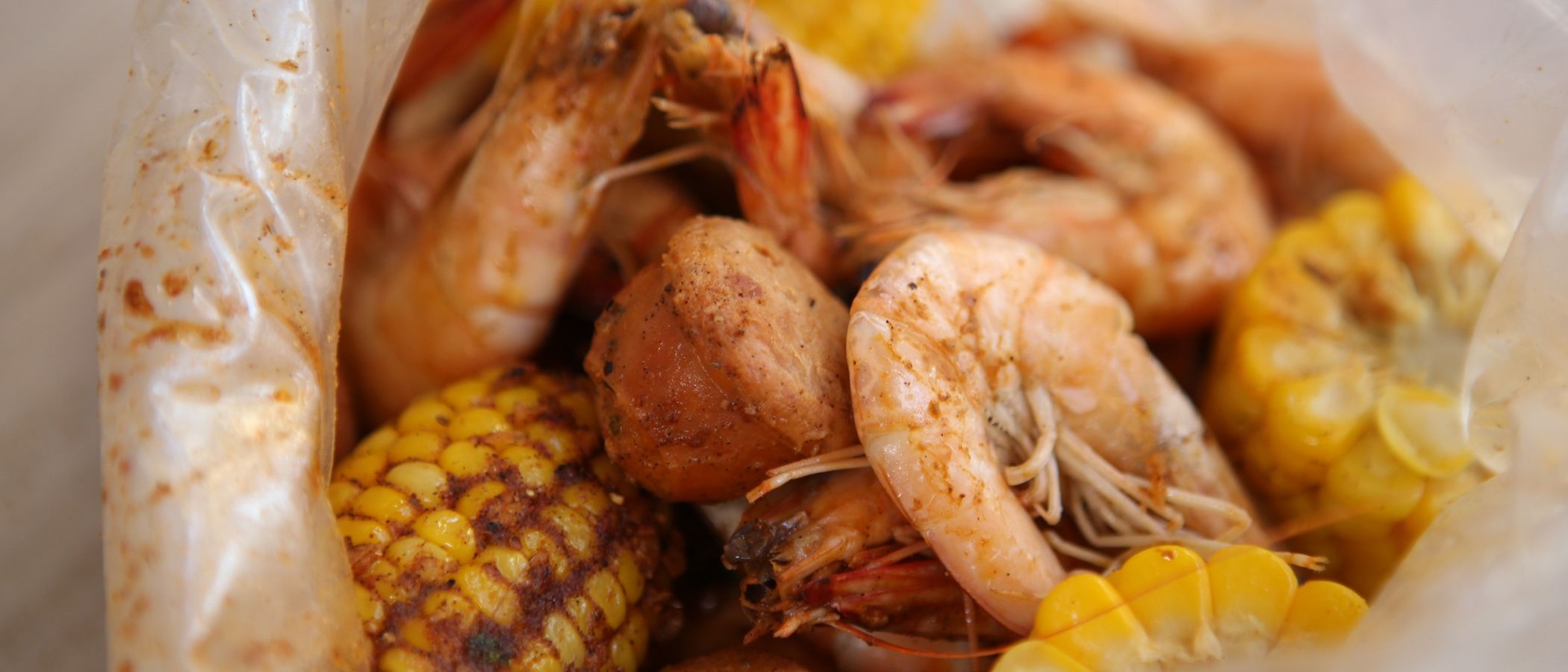 A close look inside an opened bag: head-on shrimp, sausage and corn dusted in spice