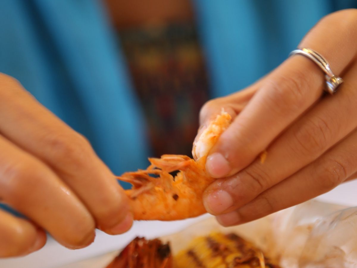 Hands peeling a boiled shrimp over an open bag of shrimp and corn