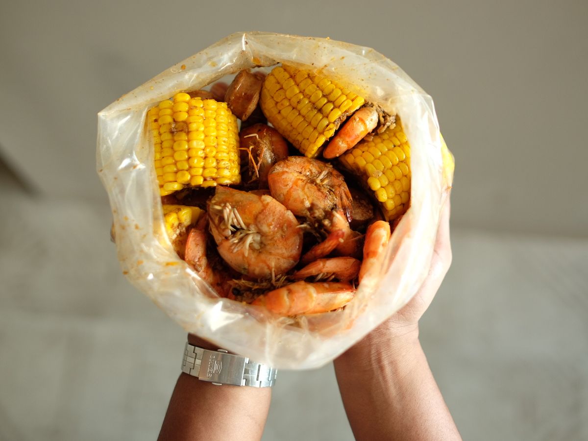 Two hands holding up an opened bag of shrimp and corn