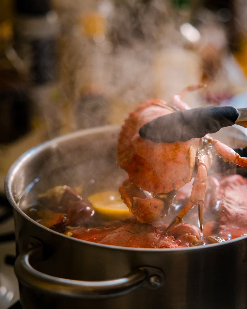 Tongs lifting a crab out of a steaming boil pot